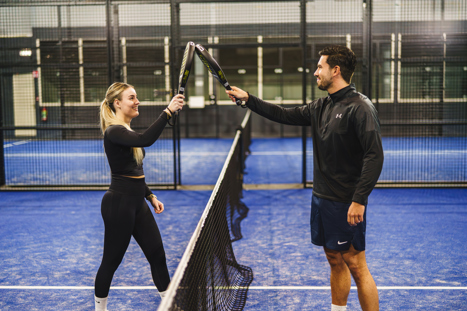 Man en vrouw geven elkaar een high five bij het net na een punt of wedstrijd op een indoor padelbaan.