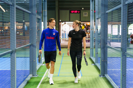 Twee spelers lopen samen richting de padelbanen, klaar om te gaan spelen.