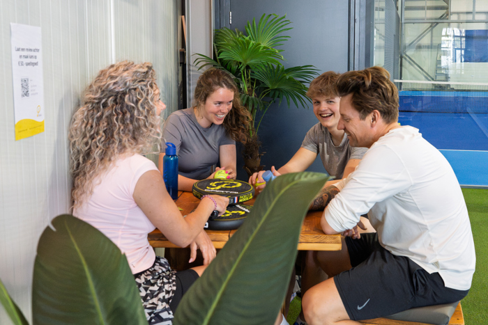 Vier mensen zitten samen aan een tafel bij Padelclub Nederland en praten tijdens een pauze tussen het padellen door.