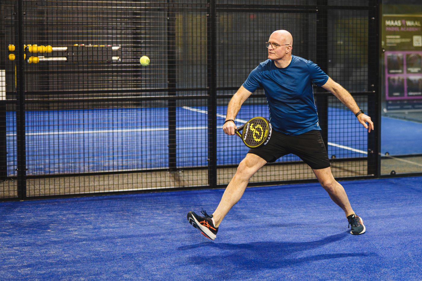Een padel speler op de indoor padelbanen in Nijmegen die de bal slaat naar zijn tegenstander