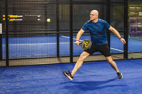 Een padel speler op de indoor padelbanen in Nijmegen die de bal slaat naar zijn tegenstander