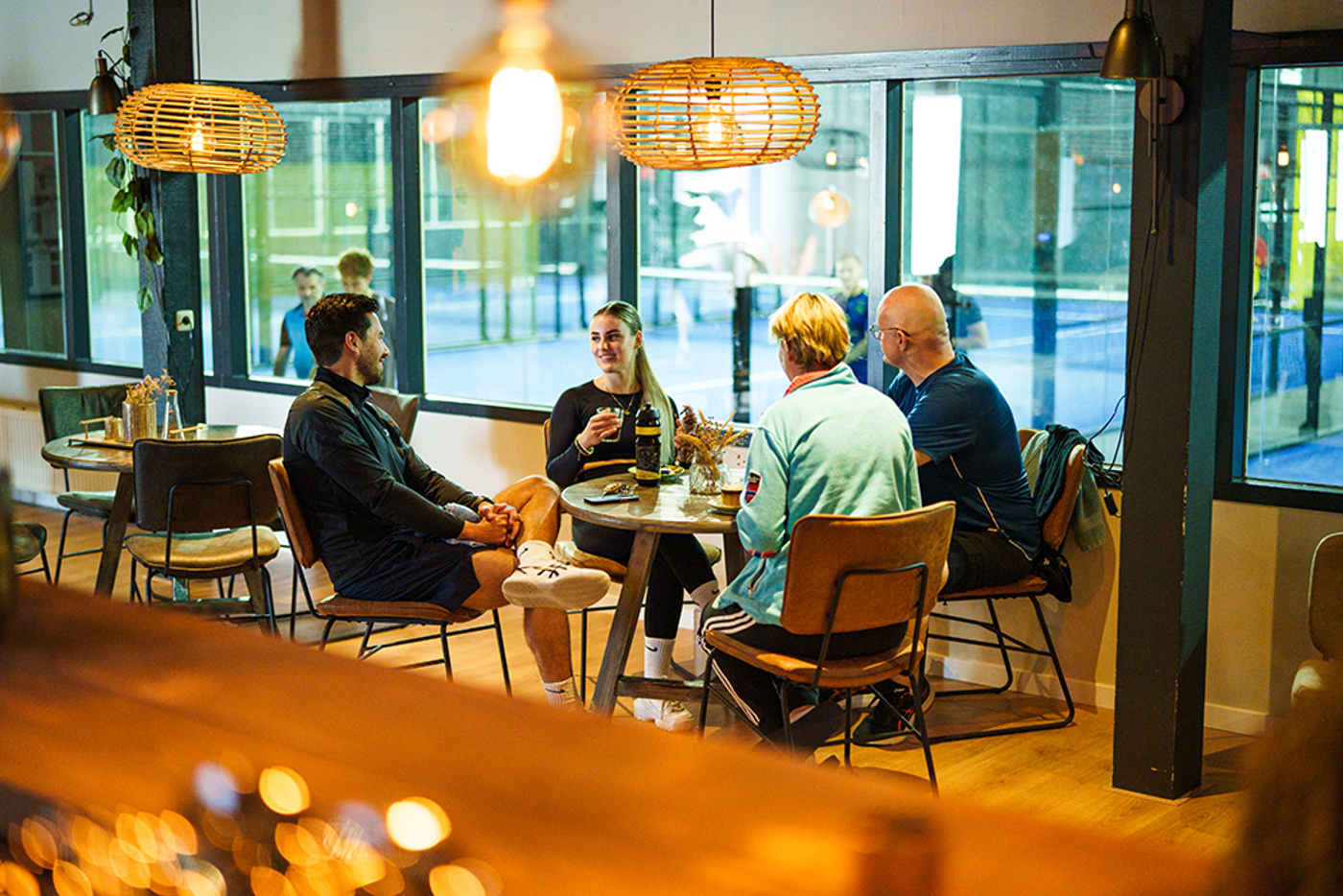 Vier padelspelers die na het padellen op de padelbanen in Nijmegen aan het kletsen zijn in het café